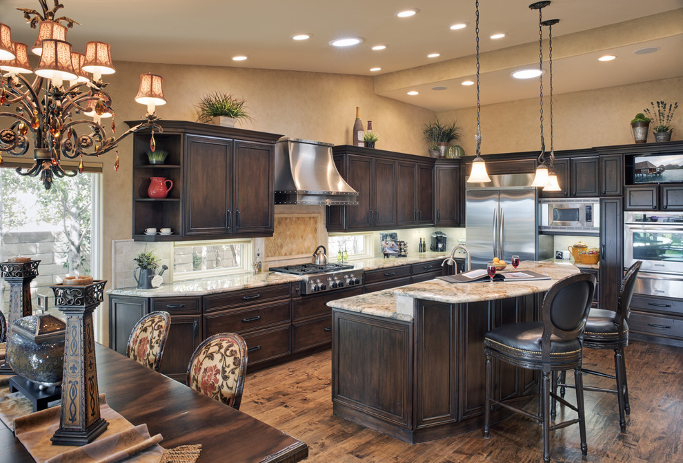 This is an example of a large classic galley open plan kitchen in Los Angeles with recessed-panel cabinets, dark wood cabinets, granite worktops, stainless steel appliances, an island, beige splashback, medium hardwood flooring and brown floors.