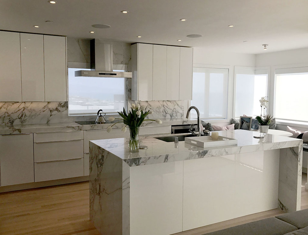 Foto på ett mellanstort funkis kök, med vita skåp, vitt stänkskydd, stänkskydd i porslinskakel, rostfria vitvaror, ljust trägolv, en köksö och beiget golv