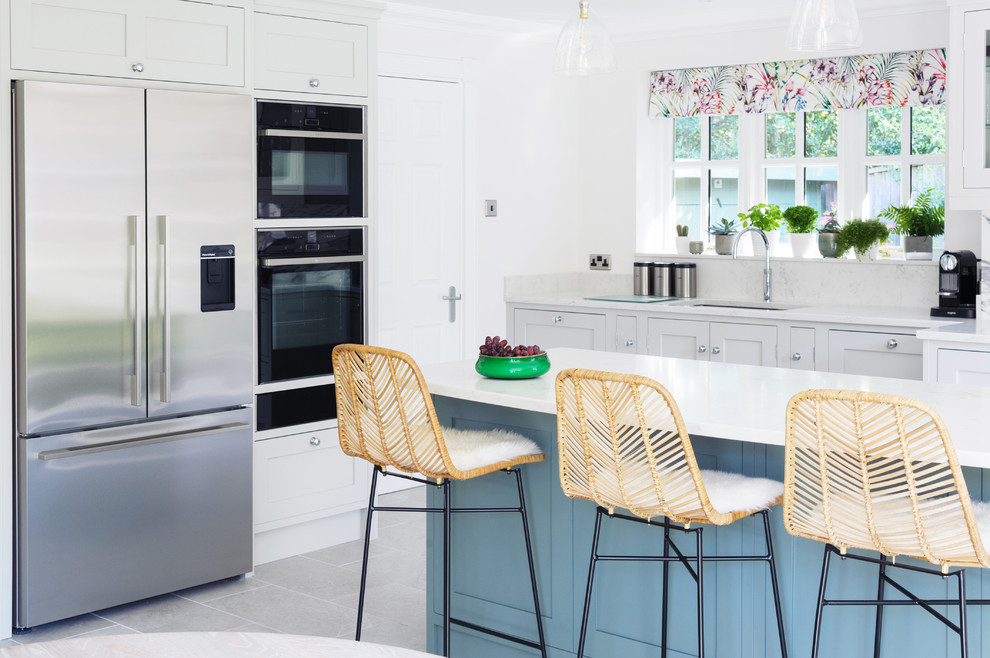 Klassische Küche in L-Form mit Unterbauwaschbecken, Schrankfronten im Shaker-Stil, blauen Schränken, Küchenrückwand in Grau, Küchengeräten aus Edelstahl, Kücheninsel, grauem Boden und weißer Arbeitsplatte in Sussex