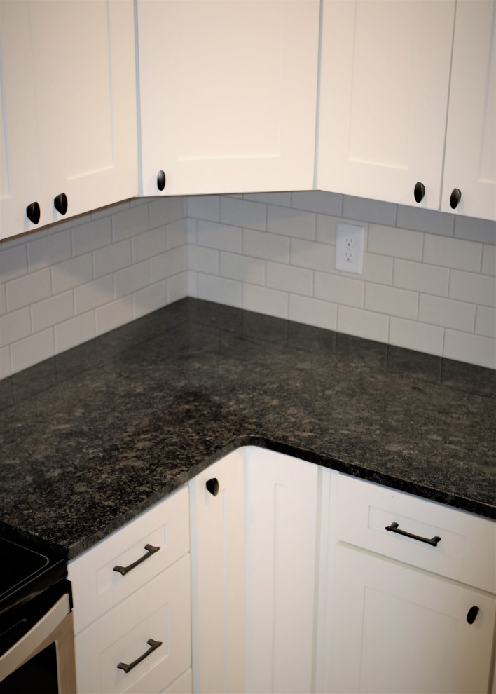 Bild på ett litet lantligt svart svart l-kök, med en nedsänkt diskho, skåp i shakerstil, vita skåp, granitbänkskiva, vitt stänkskydd, stänkskydd i tunnelbanekakel, rostfria vitvaror, klinkergolv i keramik och vitt golv