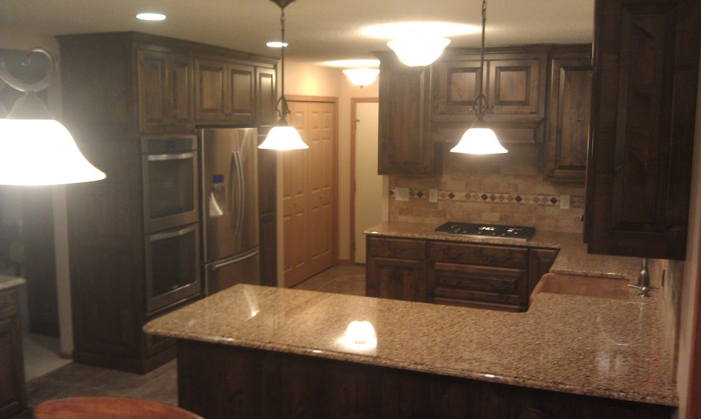 This is an example of a traditional kitchen/diner in Minneapolis with a belfast sink, raised-panel cabinets, dark wood cabinets, granite worktops, stone tiled splashback, stainless steel appliances and ceramic flooring.