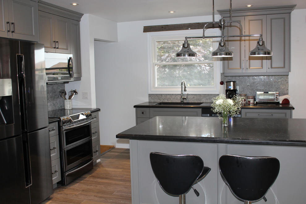 Open concept kitchen - mid-sized contemporary l-shaped vinyl floor and beige floor open concept kitchen idea in Toronto with beaded inset cabinets, gray cabinets, mosaic tile backsplash, black appliances, an island, an undermount sink, gray backsplash and black countertops