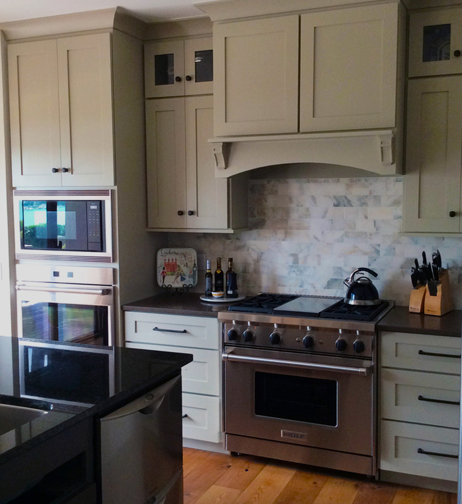 Klassisk inredning av ett mellanstort kök, med en undermonterad diskho, skåp i shakerstil, vita skåp, granitbänkskiva, vitt stänkskydd, stänkskydd i stenkakel, rostfria vitvaror, en köksö, mörkt trägolv och brunt golv