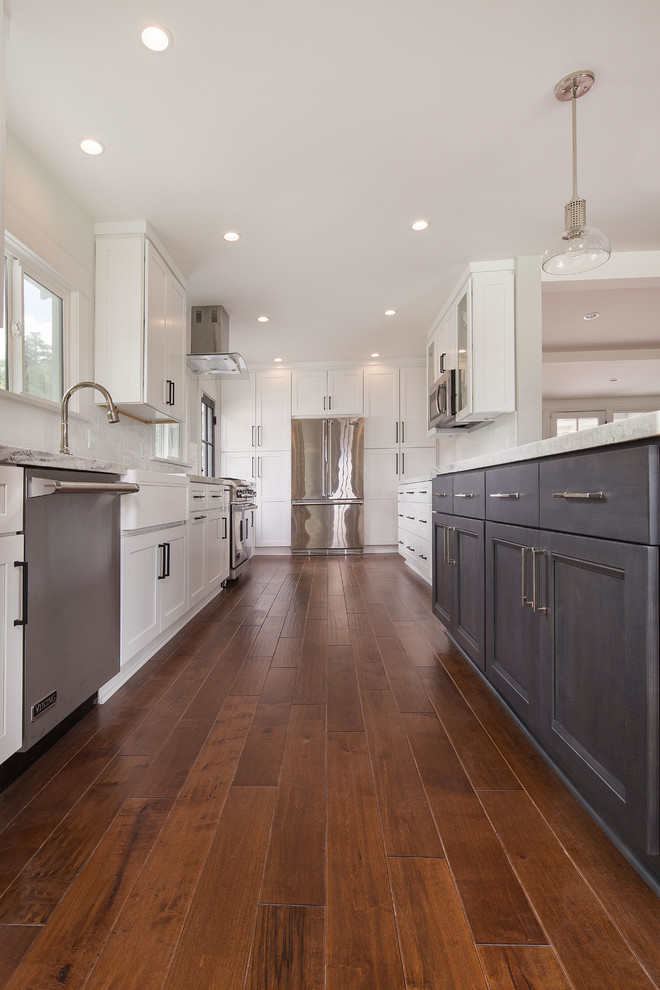 Bild på ett mellanstort vintage grå grått kök, med en rustik diskho, skåp i shakerstil, vita skåp, bänkskiva i kvartsit, vitt stänkskydd, stänkskydd i porslinskakel, rostfria vitvaror, mellanmörkt trägolv, en köksö och brunt golv