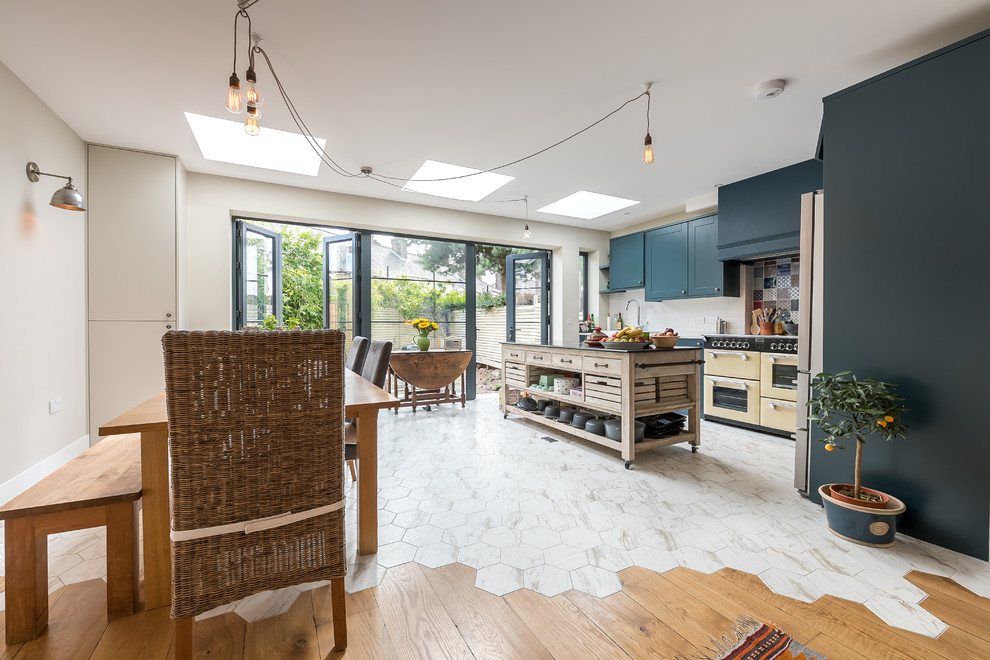 Mittelgroße Moderne Wohnküche in L-Form mit Landhausspüle, blauen Schränken, Küchenrückwand in Blau, Rückwand aus Keramikfliesen, Kücheninsel und buntem Boden in London