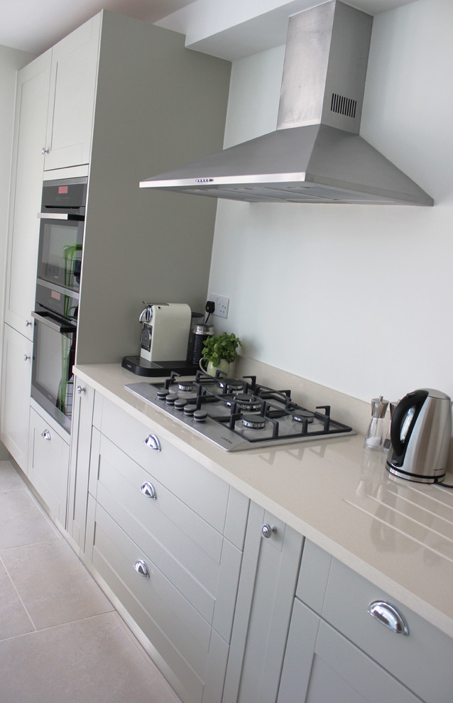 Inspiration for a large contemporary single-wall open plan kitchen in Kent with a submerged sink, shaker cabinets, grey cabinets, quartz worktops, white splashback, stainless steel appliances, porcelain flooring and an island.