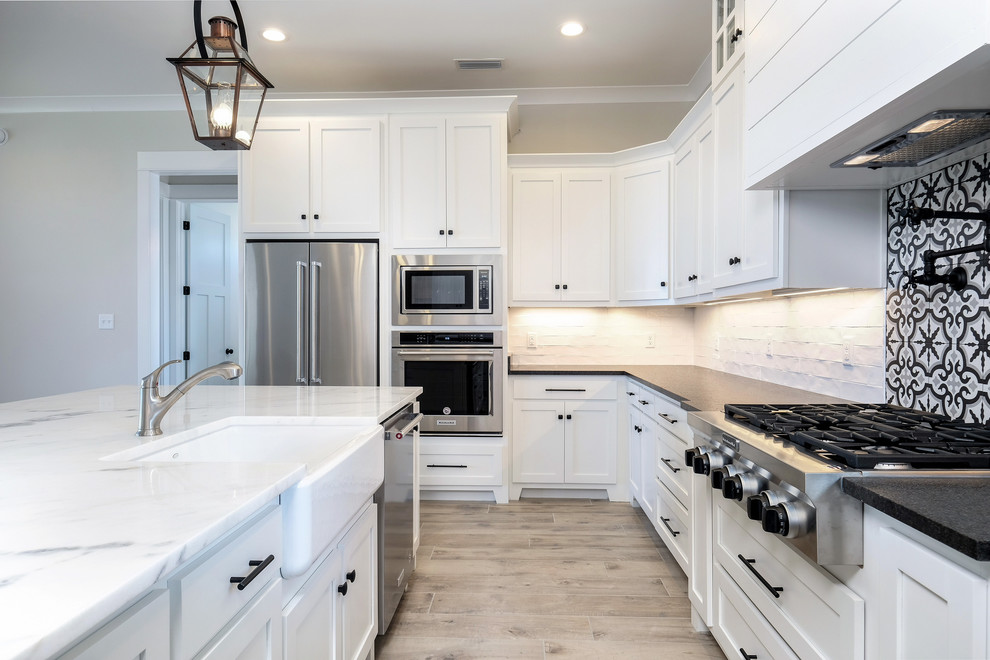 Eat-in kitchen - large coastal u-shaped light wood floor and brown floor eat-in kitchen idea in New Orleans with a farmhouse sink, shaker cabinets, white cabinets, quartz countertops, white backsplash, subway tile backsplash, stainless steel appliances, an island and gray countertops