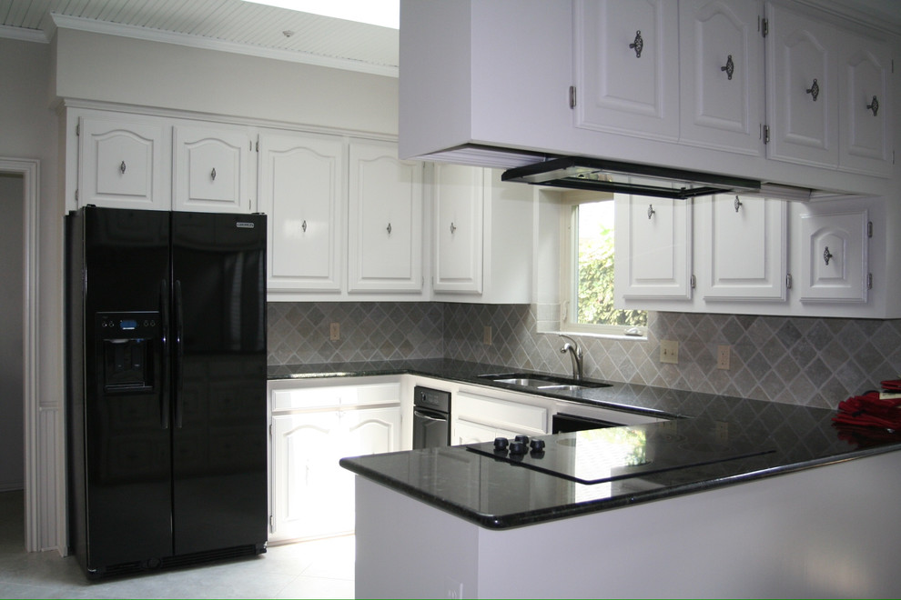 Inredning av ett klassiskt mellanstort u-kök, med en dubbel diskho, vita skåp, granitbänkskiva, grått stänkskydd, stänkskydd i stenkakel och svarta vitvaror