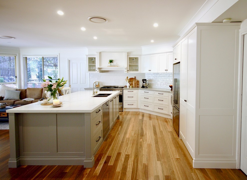 Exempel på ett stort klassiskt vit vitt kök, med en undermonterad diskho, skåp i shakerstil, grå skåp, bänkskiva i kvarts, vitt stänkskydd, stänkskydd i porslinskakel, rostfria vitvaror, mellanmörkt trägolv, en köksö och brunt golv