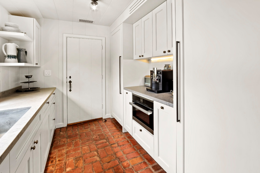Exemple d'une grande arrière-cuisine craftsman en U avec un évier encastré, un placard avec porte à panneau encastré, des portes de placard blanches, un électroménager en acier inoxydable, un sol en brique et un plan de travail gris.
