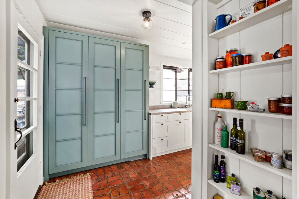 Imagen de cocina lineal de estilo americano de tamaño medio con despensa, armarios estilo shaker, puertas de armario azules, suelo de ladrillo y encimeras grises