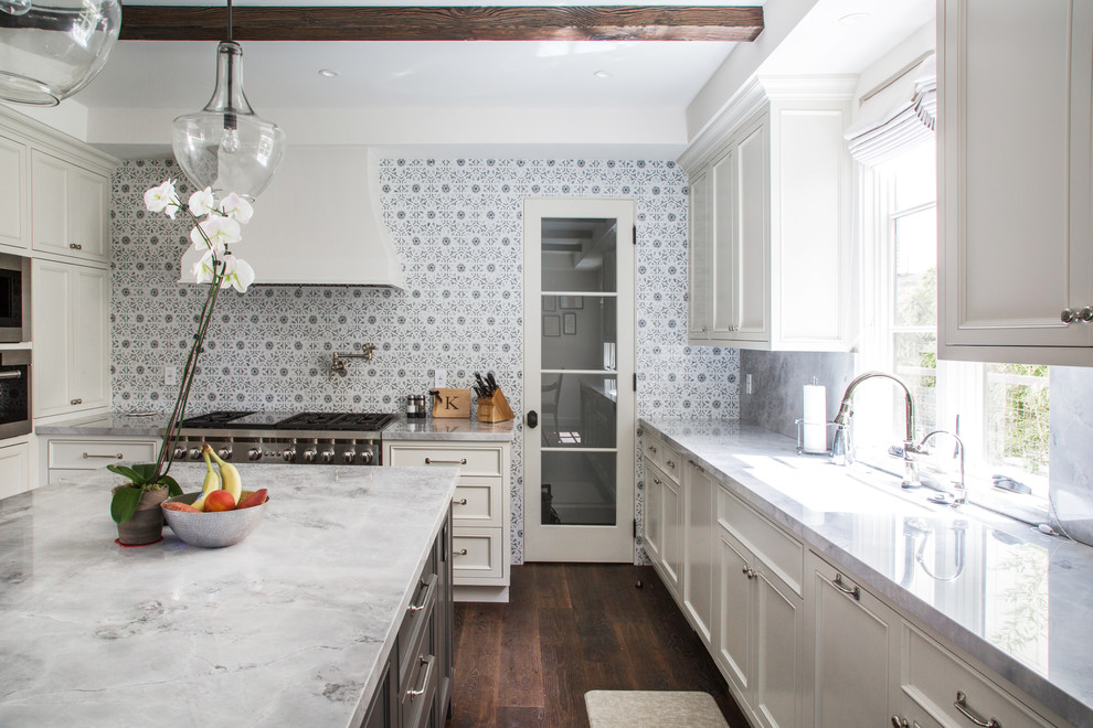 Inredning av ett medelhavsstil u-kök, med en undermonterad diskho, luckor med infälld panel, vita skåp, flerfärgad stänkskydd, rostfria vitvaror, mörkt trägolv och en köksö