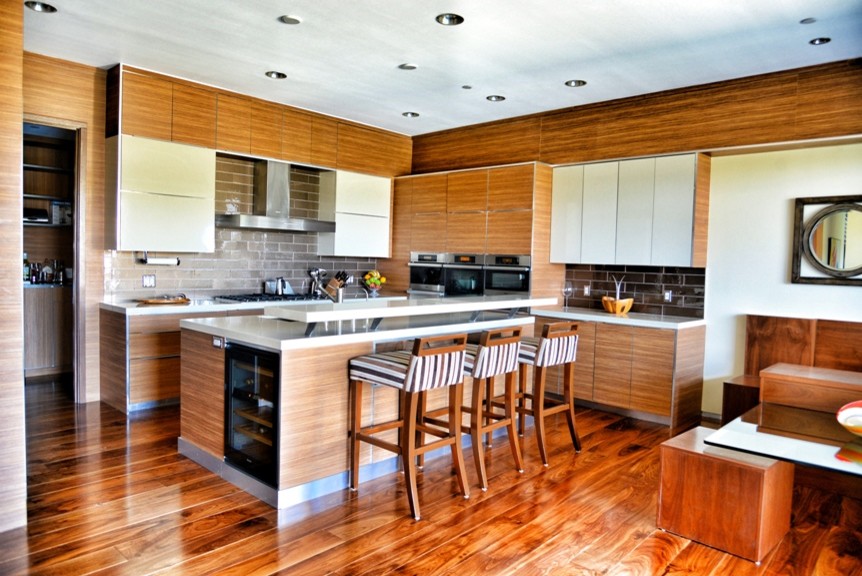 Example of a large trendy l-shaped medium tone wood floor open concept kitchen design in Los Angeles with a drop-in sink, flat-panel cabinets, light wood cabinets, solid surface countertops, black backsplash, porcelain backsplash, white appliances and an island