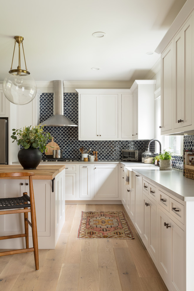 Photo of a coastal kitchen in Boston with a belfast sink, shaker cabinets, white cabinets, wood worktops, blue splashback, ceramic splashback and light hardwood flooring.