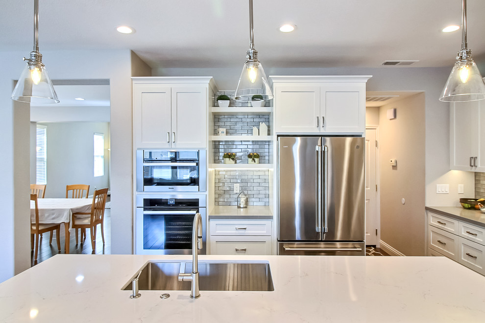 Modern inredning av ett mellanstort grå grått kök, med en enkel diskho, skåp i shakerstil, vita skåp, bänkskiva i koppar, grått stänkskydd, stänkskydd i tunnelbanekakel, rostfria vitvaror, mellanmörkt trägolv, en köksö och brunt golv