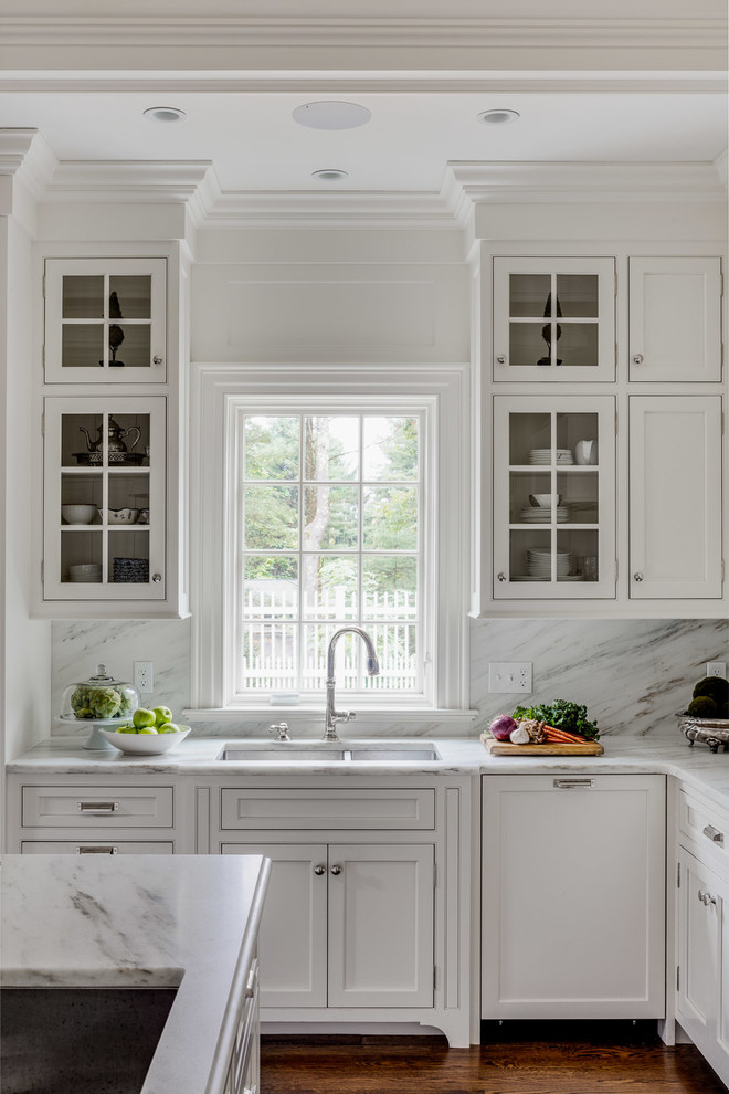 Inspiration för mellanstora lantliga vitt kök, med en nedsänkt diskho, luckor med infälld panel, vita skåp, marmorbänkskiva, vitt stänkskydd, stänkskydd i marmor, integrerade vitvaror, mellanmörkt trägolv, en köksö och brunt golv
