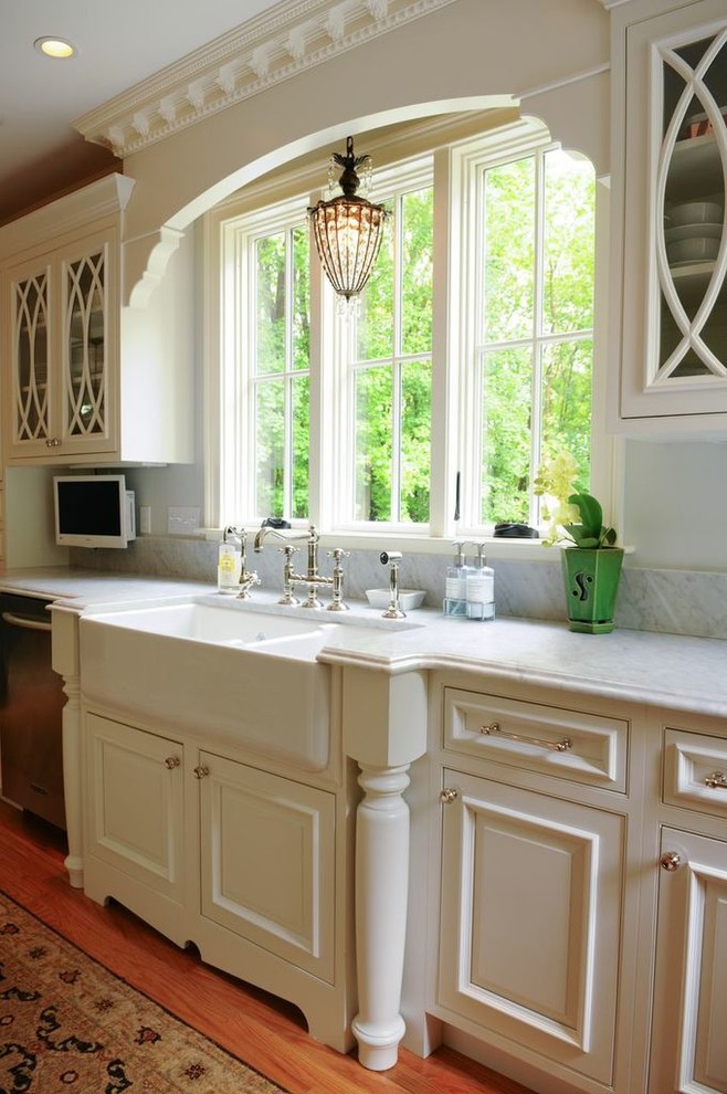 Large elegant l-shaped light wood floor eat-in kitchen photo in Boston with a farmhouse sink, raised-panel cabinets, white cabinets, marble countertops, subway tile backsplash, stainless steel appliances, white backsplash and an island