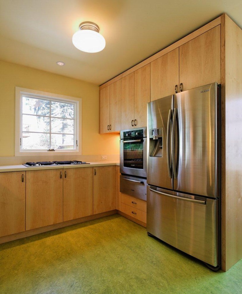 На фото: угловая кухня в стиле неоклассика (современная классика) с обеденным столом, плоскими фасадами, светлыми деревянными фасадами, столешницей из бетона и зеленым полом с