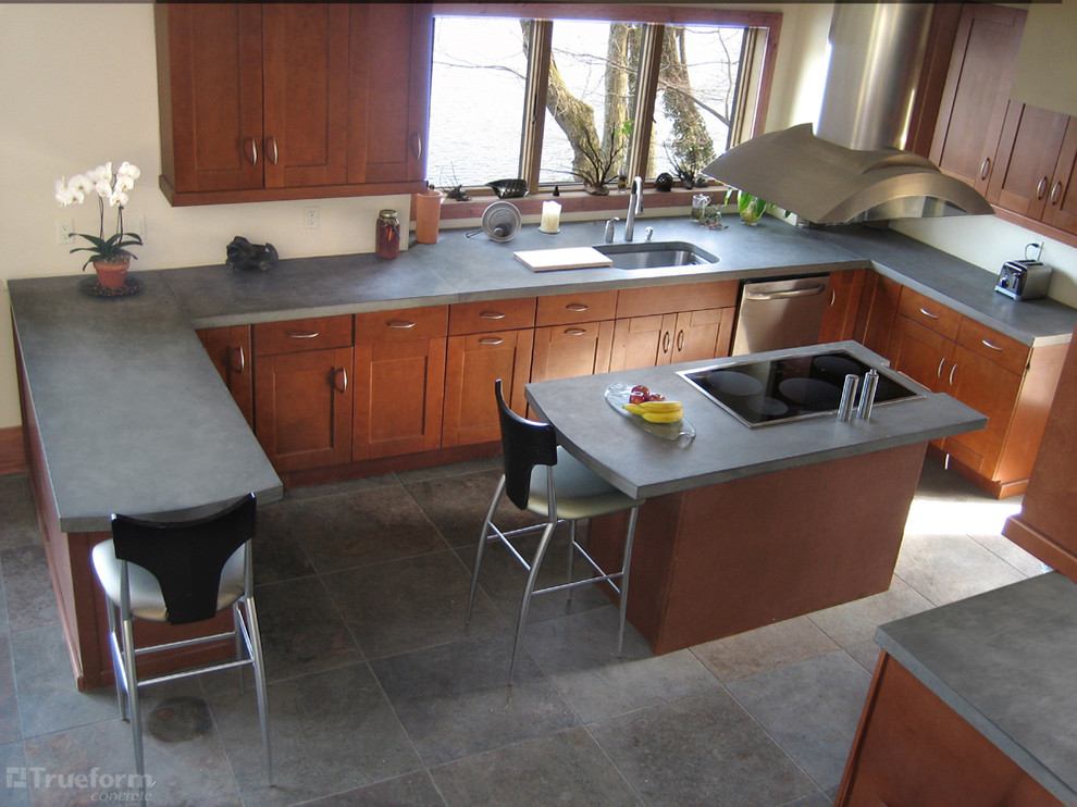 Foto på ett stort funkis kök, med en nedsänkt diskho, bänkskiva i betong, ljust trägolv och en köksö