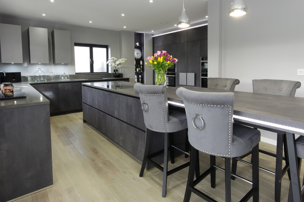 Large contemporary l-shaped kitchen/diner in Kent with grey cabinets, black appliances, a breakfast bar, grey worktops, a built-in sink, flat-panel cabinets and beige floors.