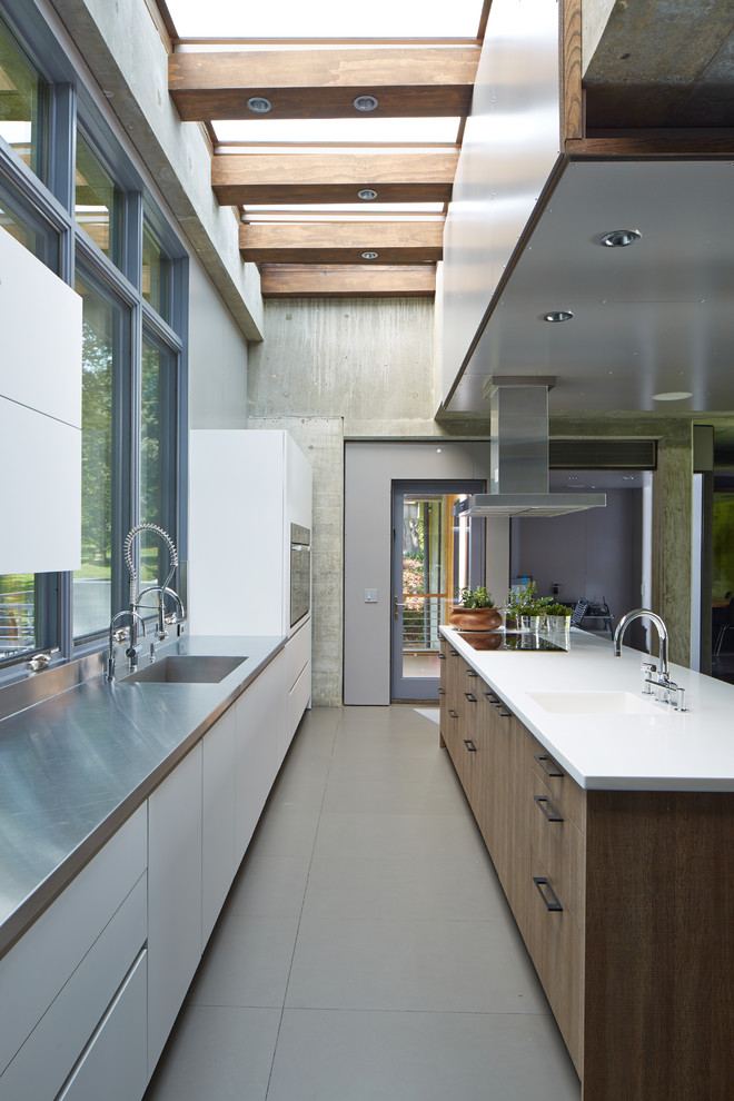This is an example of a large contemporary single-wall kitchen in New York with a single-bowl sink, flat-panel cabinets, white cabinets, stainless steel worktops, cement flooring and an island.