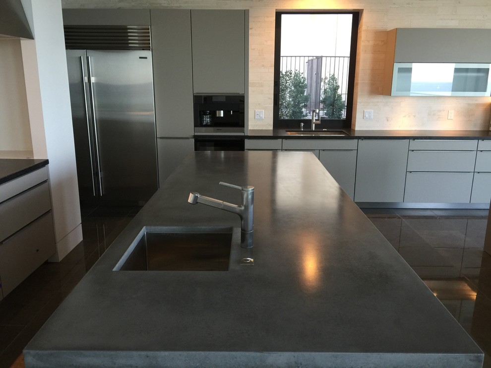 Modern inredning av ett kök, med släta luckor, grå skåp, bänkskiva i betong, beige stänkskydd, stänkskydd i sten, rostfria vitvaror och en köksö