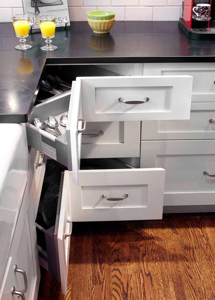 Photo of a medium sized industrial l-shaped kitchen/diner in Montreal with a belfast sink, shaker cabinets, white cabinets, granite worktops, white splashback, metro tiled splashback, stainless steel appliances, medium hardwood flooring and an island.