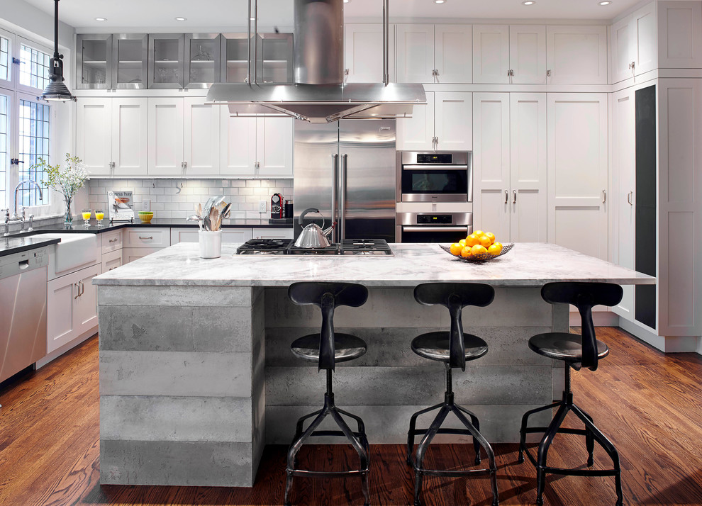 Eat-in kitchen - mid-sized industrial l-shaped medium tone wood floor eat-in kitchen idea in Montreal with a farmhouse sink, shaker cabinets, white cabinets, granite countertops, white backsplash, subway tile backsplash, stainless steel appliances and an island