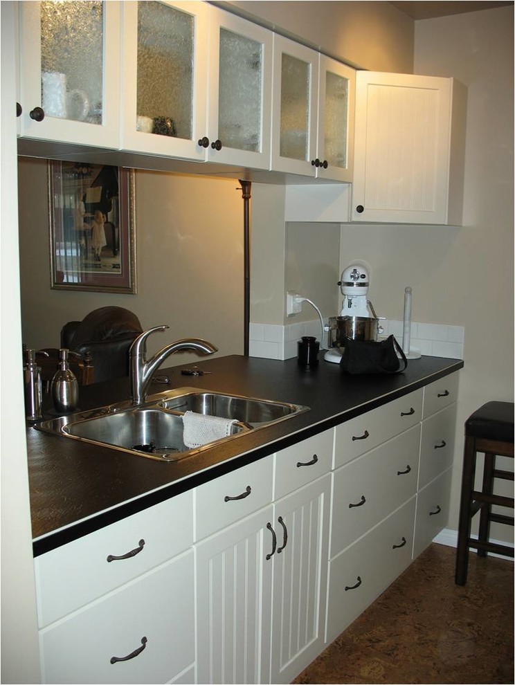 Foto på ett litet funkis kök, med en nedsänkt diskho, luckor med glaspanel, beige skåp, laminatbänkskiva, vitt stänkskydd, stänkskydd i keramik, vita vitvaror och korkgolv