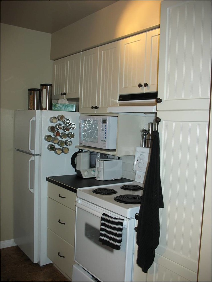 Example of a small minimalist galley cork floor eat-in kitchen design in Other with glass-front cabinets, beige cabinets, laminate countertops, no island, a drop-in sink, white backsplash, white appliances and subway tile backsplash