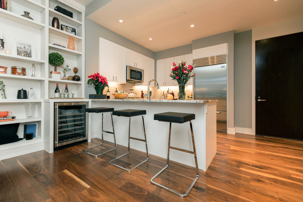 Idées déco pour une petite cuisine américaine moderne en L avec un placard à porte shaker, des portes de placard blanches, plan de travail en marbre, une crédence beige, un électroménager en acier inoxydable, un sol en bois brun, îlot, un sol marron et un plan de travail gris.