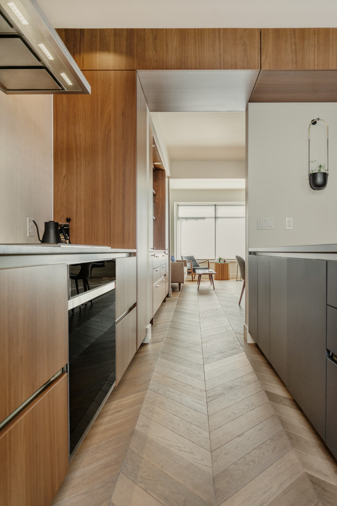 Inspiration pour une petite cuisine parallèle minimaliste en bois brun fermée avec un évier encastré, un électroménager noir, parquet clair, une péninsule, un plan de travail gris et un placard à porte plane.