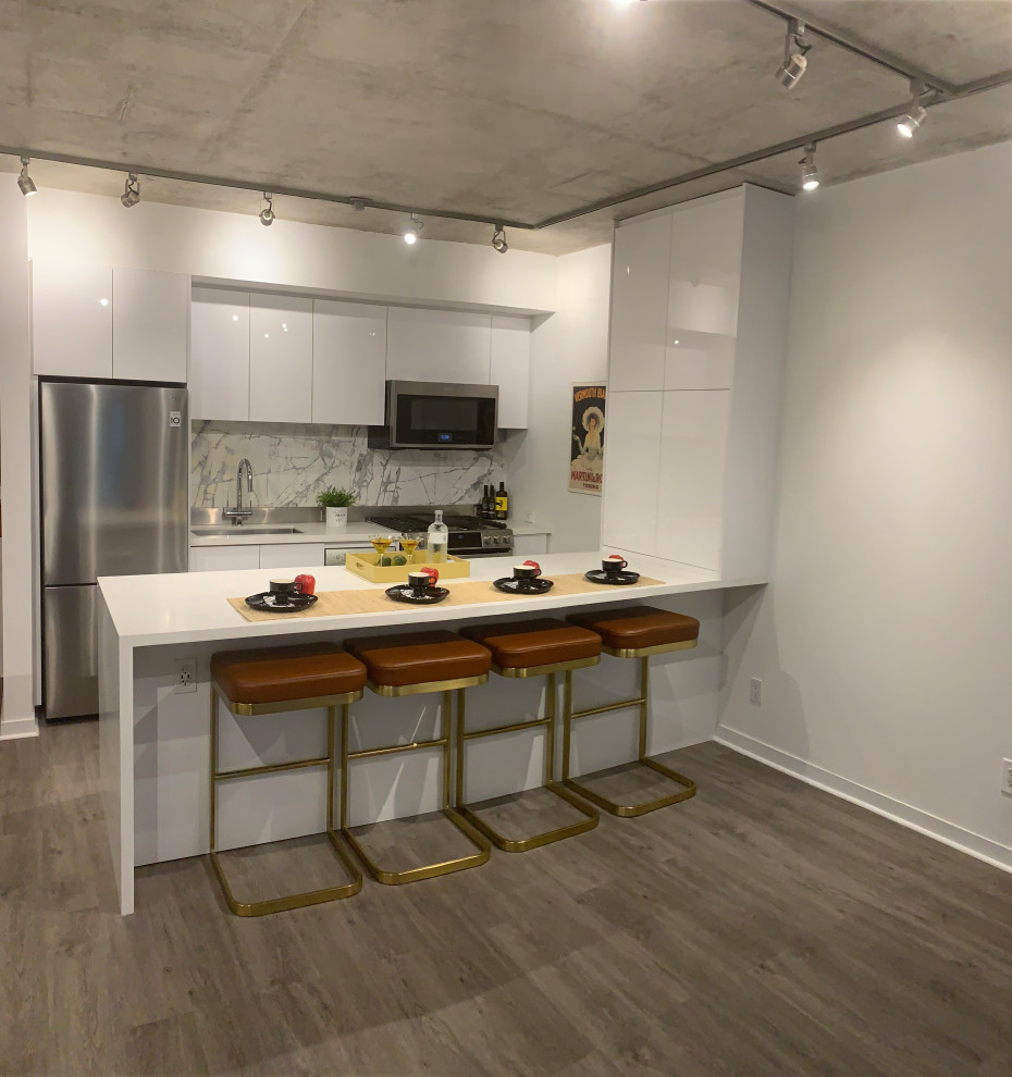 Modern inredning av ett litet vit vitt kök, med en undermonterad diskho, släta luckor, vita skåp, bänkskiva i kvarts, grått stänkskydd, stänkskydd i stenkakel, rostfria vitvaror, vinylgolv, en köksö och grått golv