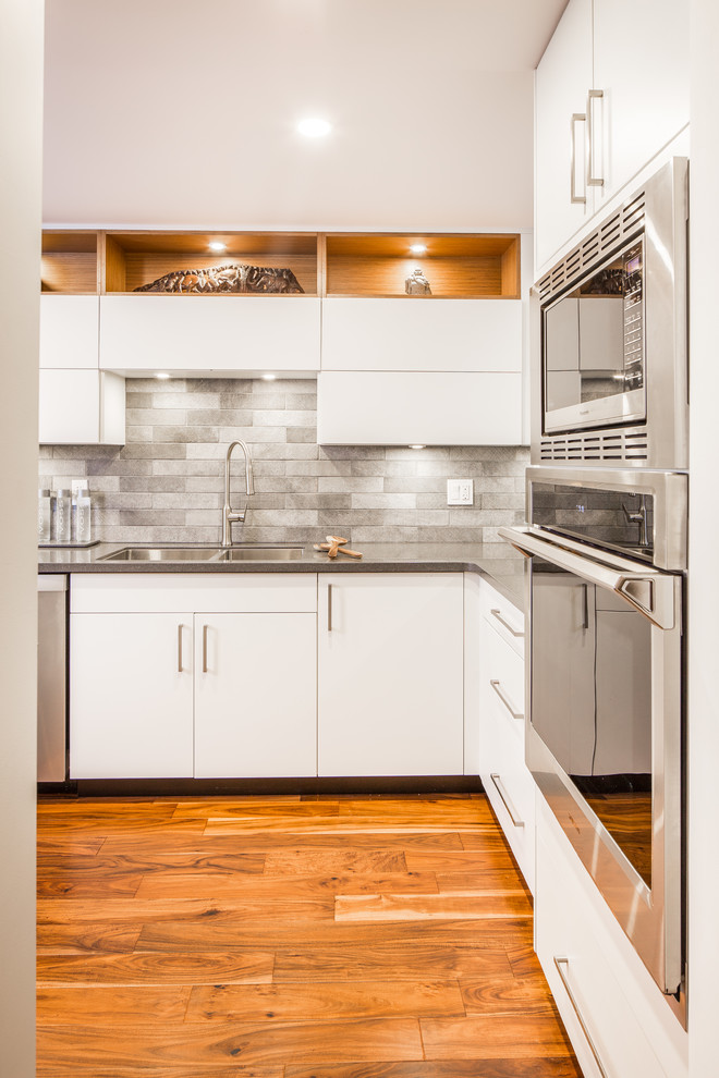 Small minimalist l-shaped medium tone wood floor and brown floor eat-in kitchen photo in Vancouver with an undermount sink, flat-panel cabinets, white cabinets, quartz countertops, gray backsplash, porcelain backsplash, stainless steel appliances, an island and gray countertops