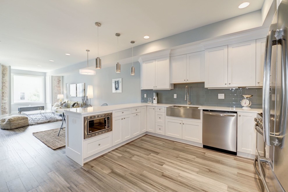 Example of a transitional u-shaped bamboo floor and brown floor open concept kitchen design in DC Metro with a farmhouse sink, shaker cabinets, white cabinets, quartz countertops, blue backsplash, glass tile backsplash, stainless steel appliances and no island