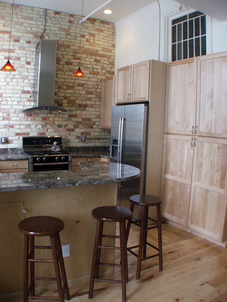 Cette image montre une cuisine américaine bohème en U et bois clair avec un évier encastré, un placard à porte shaker, un plan de travail en granite et un électroménager en acier inoxydable.