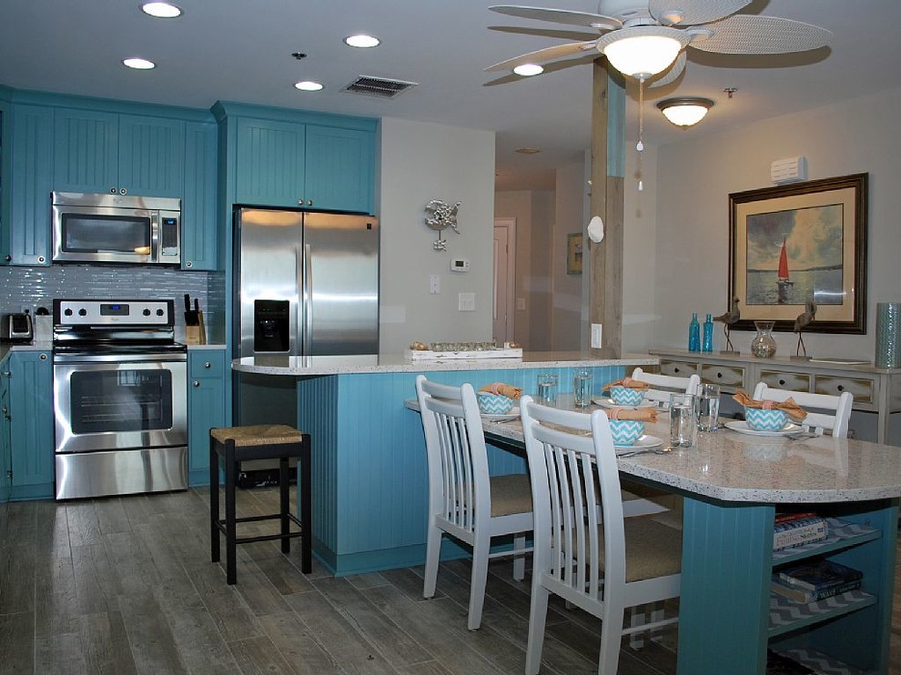 Cette photo montre une cuisine américaine parallèle bord de mer avec un placard avec porte à panneau encastré, des portes de placard turquoises, un plan de travail en granite et 2 îlots.