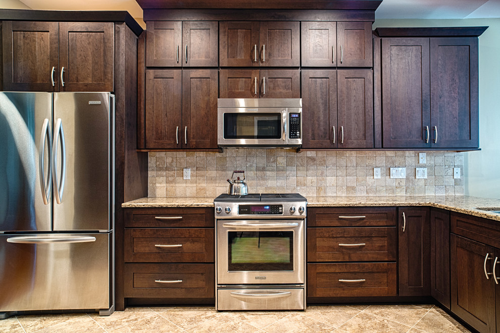 Aménagement d'une cuisine américaine classique en U et bois foncé de taille moyenne avec un évier encastré, un placard à porte shaker, un plan de travail en quartz modifié, une crédence beige, une crédence en carrelage de pierre, un électroménager en acier inoxydable, un sol en carrelage de céramique, îlot et un sol beige.