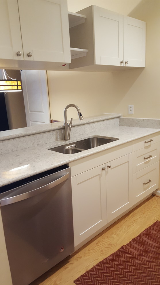Inspiration for a small traditional galley open plan kitchen in Grand Rapids with a submerged sink, shaker cabinets, white cabinets, quartz worktops, stainless steel appliances, light hardwood flooring, a breakfast bar and brown floors.