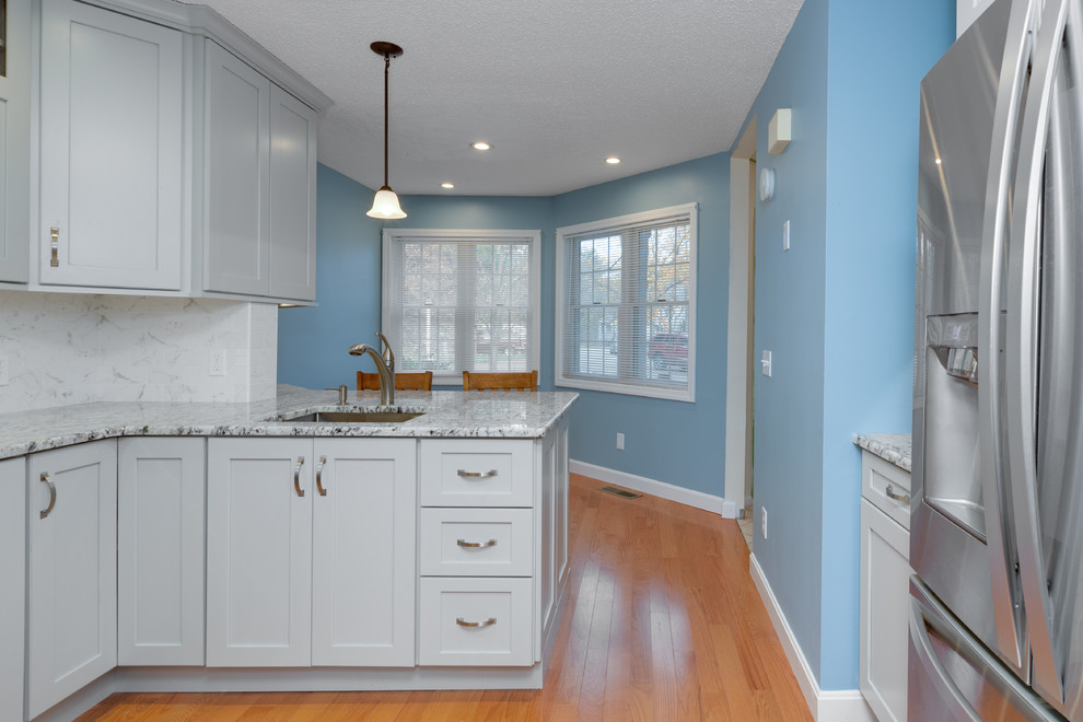 Inspiration for a mid-sized transitional u-shaped medium tone wood floor eat-in kitchen remodel in Boston with an undermount sink, shaker cabinets, gray cabinets, granite countertops, stone tile backsplash, stainless steel appliances and a peninsula