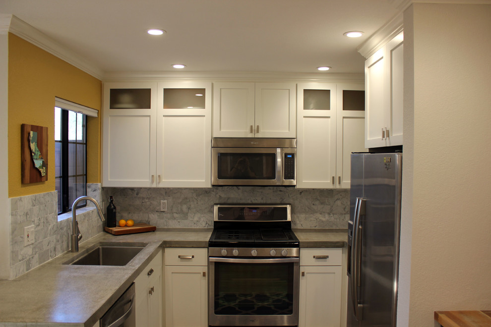 Bild på ett litet funkis kök, med en undermonterad diskho, skåp i shakerstil, vita skåp, bänkskiva i betong, grått stänkskydd, stänkskydd i stenkakel, rostfria vitvaror och ljust trägolv