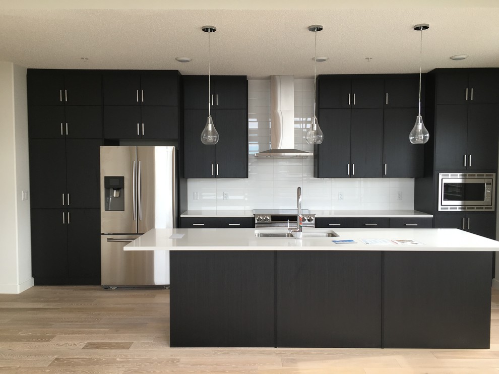 Eat-in kitchen - mid-sized modern galley light wood floor eat-in kitchen idea in Calgary with an undermount sink, flat-panel cabinets, black cabinets, white backsplash, subway tile backsplash, stainless steel appliances, an island and quartz countertops