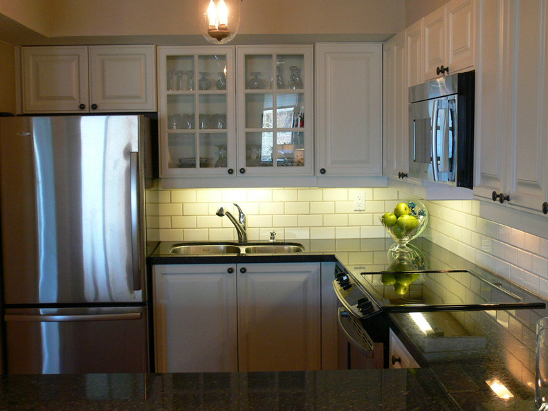 This is an example of a large traditional u-shaped enclosed kitchen in Toronto with a submerged sink, raised-panel cabinets, white cabinets, granite worktops, white splashback, metro tiled splashback, stainless steel appliances and a breakfast bar.