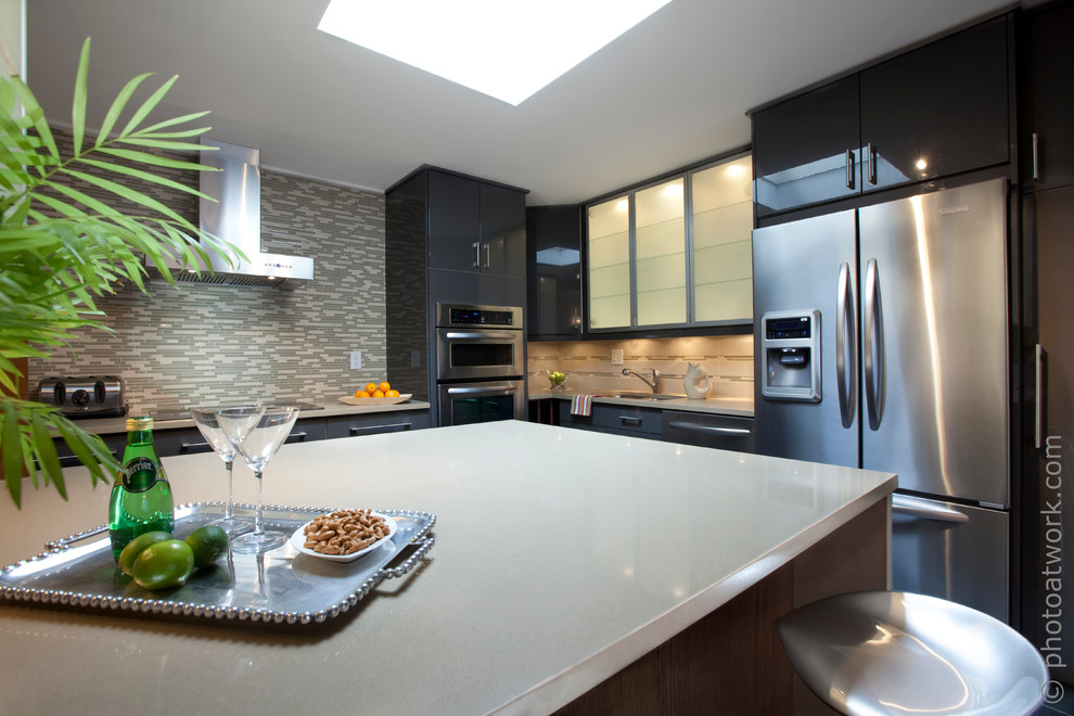 Medium sized contemporary l-shaped open plan kitchen in Montreal with a submerged sink, flat-panel cabinets, engineered stone countertops, grey splashback, glass tiled splashback, stainless steel appliances, porcelain flooring and an island.