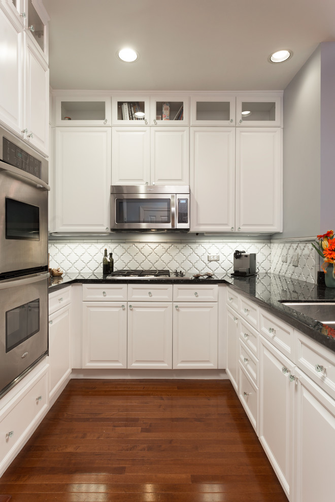 Inspiration for a mid-sized contemporary u-shaped medium tone wood floor enclosed kitchen remodel in Chicago with an undermount sink, shaker cabinets, white cabinets, granite countertops, white backsplash, ceramic backsplash, stainless steel appliances and no island