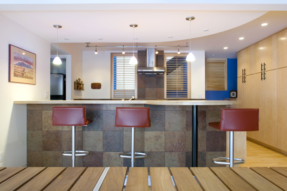 Cette image montre une cuisine parallèle design en bois clair avec un placard à porte plane, un électroménager en acier inoxydable, un plan de travail en bois, une crédence marron et une crédence en carrelage de pierre.