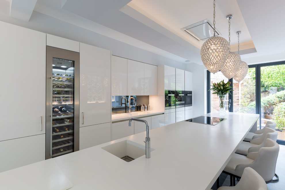 Design ideas for a medium sized contemporary open plan kitchen in Cheshire with flat-panel cabinets, white cabinets, grey splashback, mirror splashback, black appliances, porcelain flooring, an island, grey floors and white worktops.