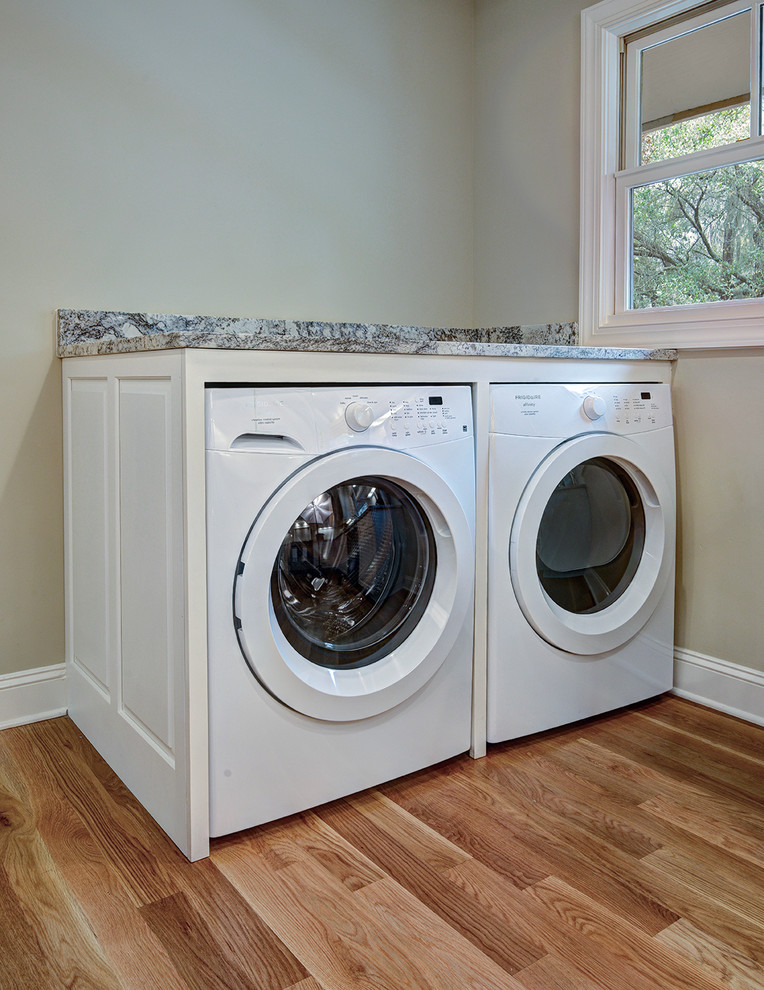Inspiration for a mid-sized transitional l-shaped light wood floor laundry room remodel in Charleston with a double-bowl sink, raised-panel cabinets, white cabinets, granite countertops, white backsplash and beige walls