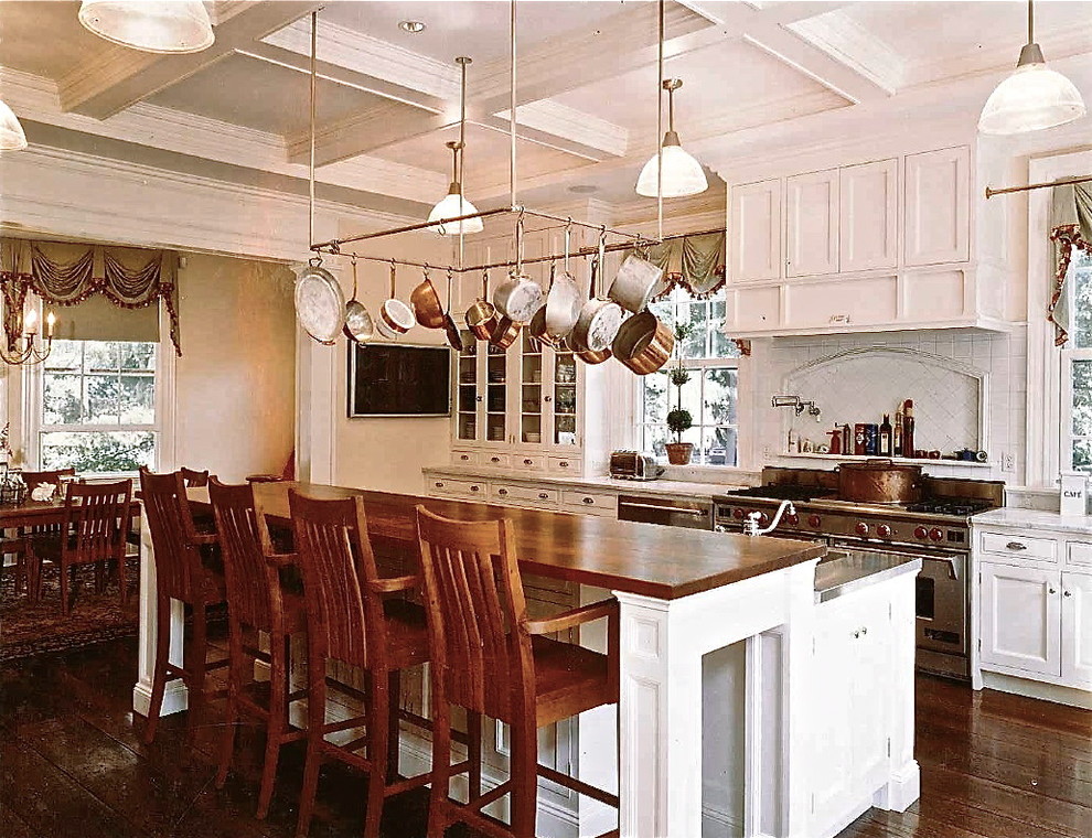 Example of a mid-sized classic l-shaped dark wood floor kitchen design in New York with a farmhouse sink, shaker cabinets, white cabinets, wood countertops, mirror backsplash and an island