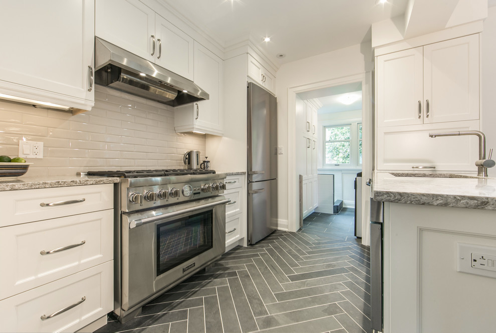Photo of a medium sized classic galley kitchen/diner in Toronto with shaker cabinets, white cabinets, stainless steel appliances, quartz worktops, a breakfast bar, a submerged sink, grey splashback, ceramic splashback and slate flooring.